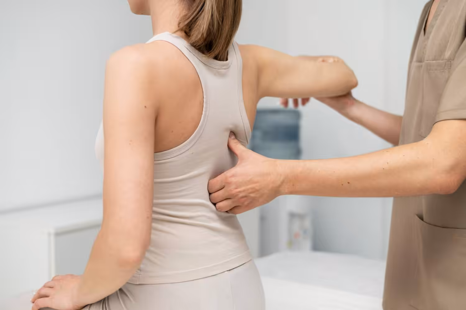 A person in light clothing is having their upper back examined by a healthcare professional in a clinical setting.