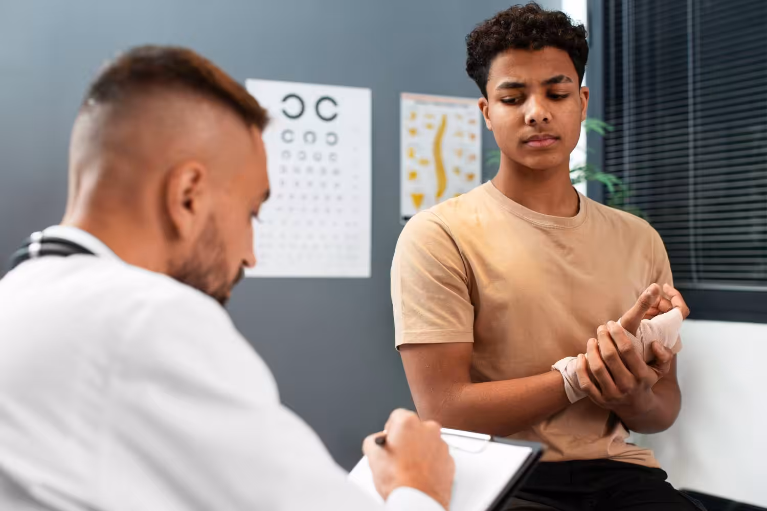 A doctor consults with a young man holding his bandaged wrist in a medical office.