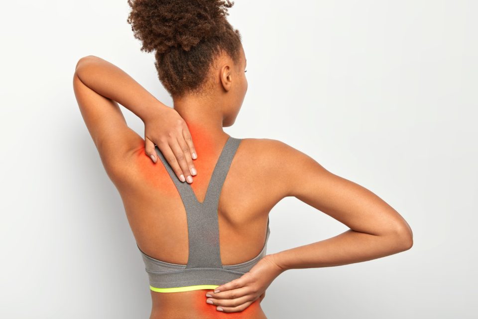 Woman in athletic wear touches her upper and lower back, with red shading indicating pain or discomfort, standing against a plain light background.